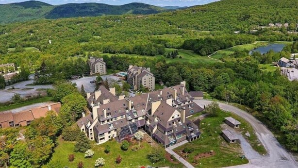 A large, multi-story building with a central courtyard, surrounded by lush greenery and hills. - Luxury Mountain Suite - Ski/Golf/Hike/Play (Killington)