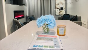 A dining table with a vase of blue flowers, a candle, and a welcome brochure. - Luxury Mountain Suite - Ski/Golf/Hike/Play (Killington)
