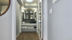 A narrow hallway leading to a bathroom with a white vanity, two mirrors, and a towel rack. - Luxury Mountain Suite - Ski/Golf/Hike/Play (Killington)
