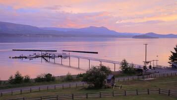 A lakeside view with a dock, a small building, and a wooden fence.