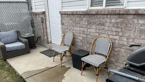 Een terras met twee rieten stoelen, een kleine tafel en een barbecue.
