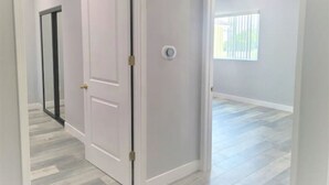 Un couloir avec une porte blanche, un thermostat et une fenĂŞtre avec des stores.