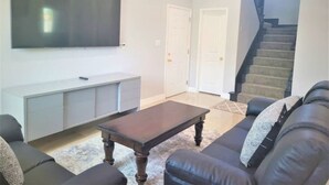 Un salon doté d’un téléviseur à écran plat, d’une table basse en bois foncé, d’un canapé en cuir et d’un escalier menant à un autre niveau.