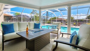 A sunroom with a pool view, a wooden table, and white cushioned seating. - VRCC Villa San Miguel (Cape Coral)