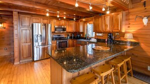 A spacious kitchen with wooden cabinets, stainless steel appliances, and a granite countertop. - Cozy Cabin Tucked Away in Wooded Property (Boone)