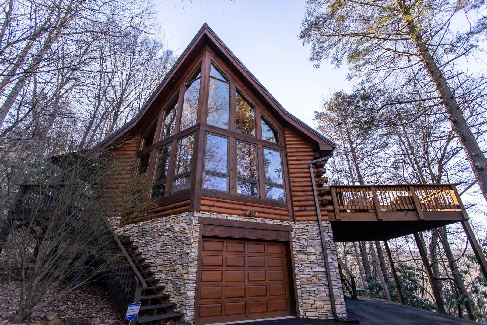 Une cabane en rondins avec des fondations en pierre, de grandes fenêtres et une terrasse en bois.