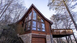 A log cabin with a stone foundation, large windows, and a wooden deck. - Cozy Cabin Tucked Away in Wooded Property (Boone)