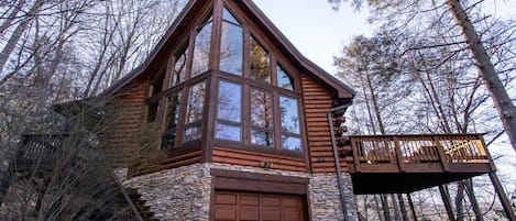 Une cabane en rondins avec des fondations en pierre, de grandes fenêtres et une terrasse en bois.