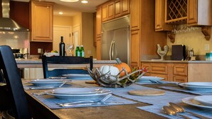 A kitchen with wooden cabinets, a stainless steel refrigerator, and a dining table set with plates, cutlery, and a decorative centerpiece. - Epic Mountain View. Luxury House on a Hill. River 10 min (Kernville)