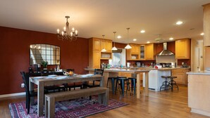 A spacious kitchen with wooden cabinets, a central island, and a dining area with a bench and chairs. - Epic Mountain View. Luxury House on a Hill. River 10 min (Kernville)