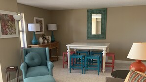 Uma sala de estar com uma mesa de centro preta, uma poltrona azul-turquesa, um sofá cinza e uma mesa de jantar azul-turquesa com quatro cadeiras.