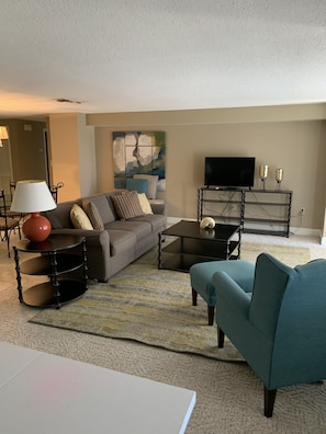 A living room with a sofa, a coffee table, a TV stand, and a lamp.