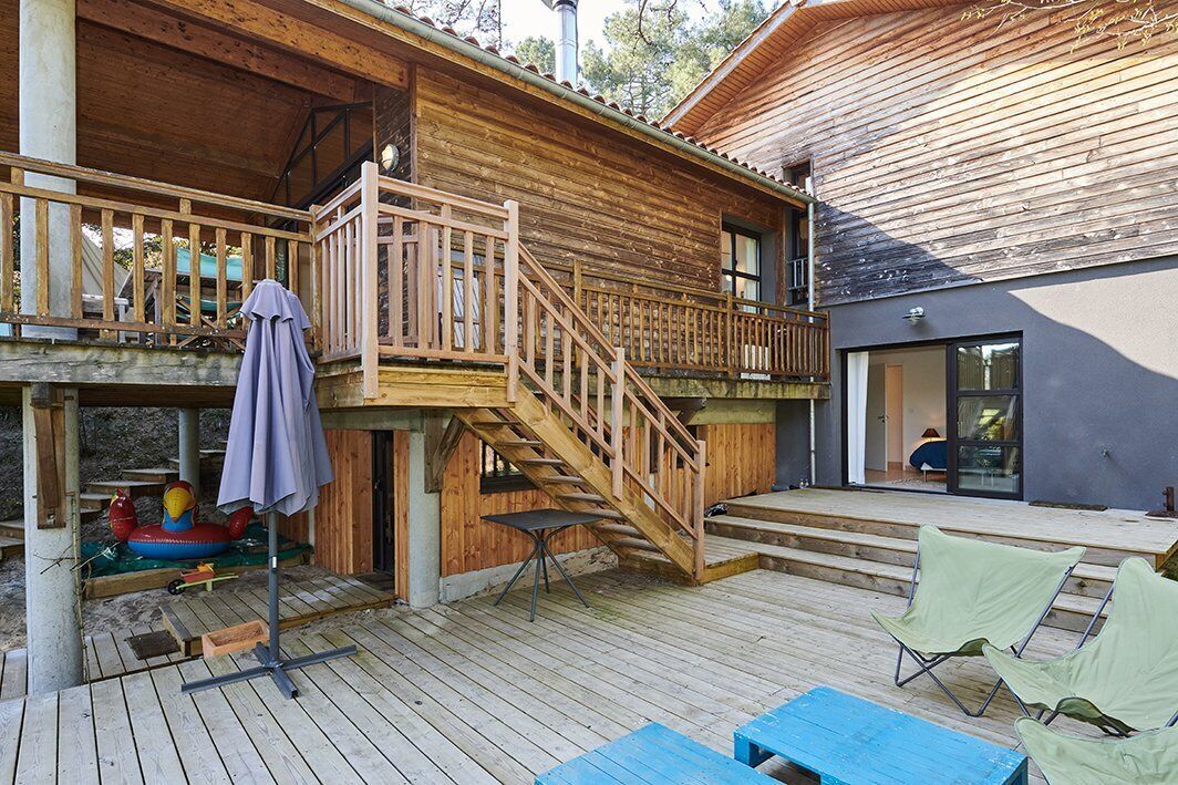 Een houten terras met een trap naar een balkon, zitplaatsen buiten en een zwembadgedeelte.