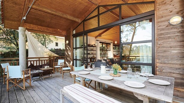 Une terrasse en bois avec une table à manger pour quatre personnes, entourée de chaises et d’un banc.