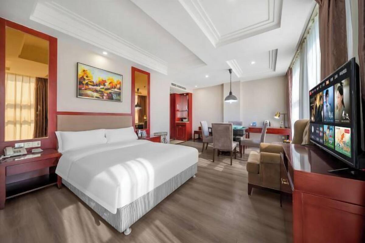 A hotel room with a large bed, a desk, a chair, a television, and a painting on the wall.