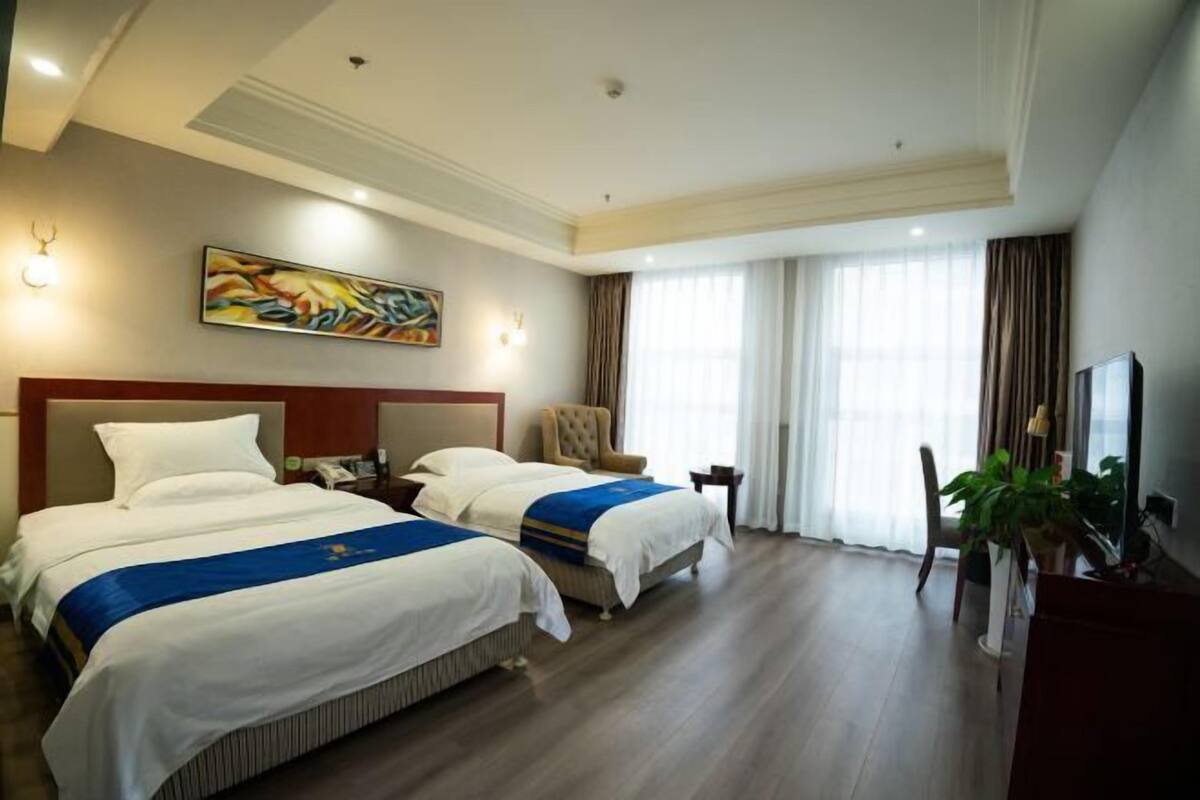 A hotel room with two beds, a large painting on the wall, a chair, a desk, and a television.