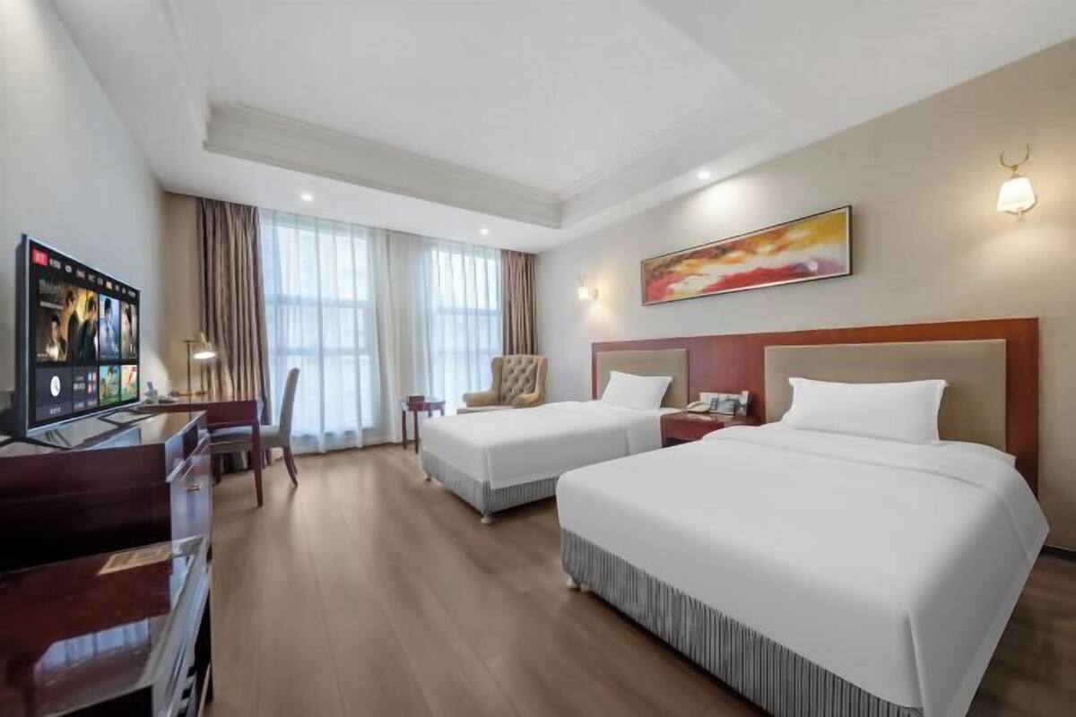 A hotel room with two beds, a desk, a chair, and a TV.