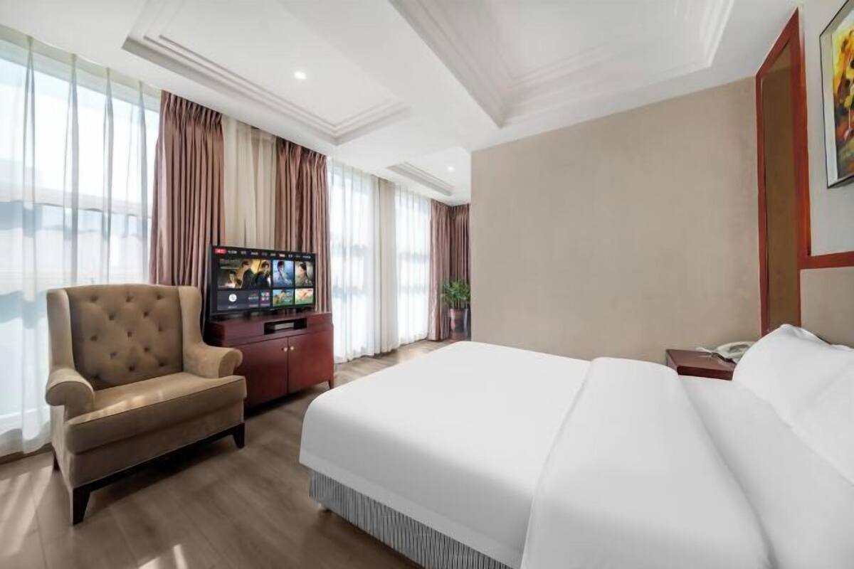 A hotel room with a large bed, a TV on a stand, a sofa, and a desk with a telephone.
