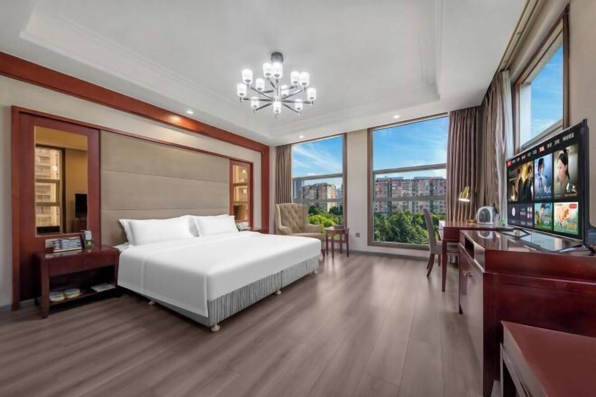 A hotel room with a large bed, a desk, a TV, and a view of the city.