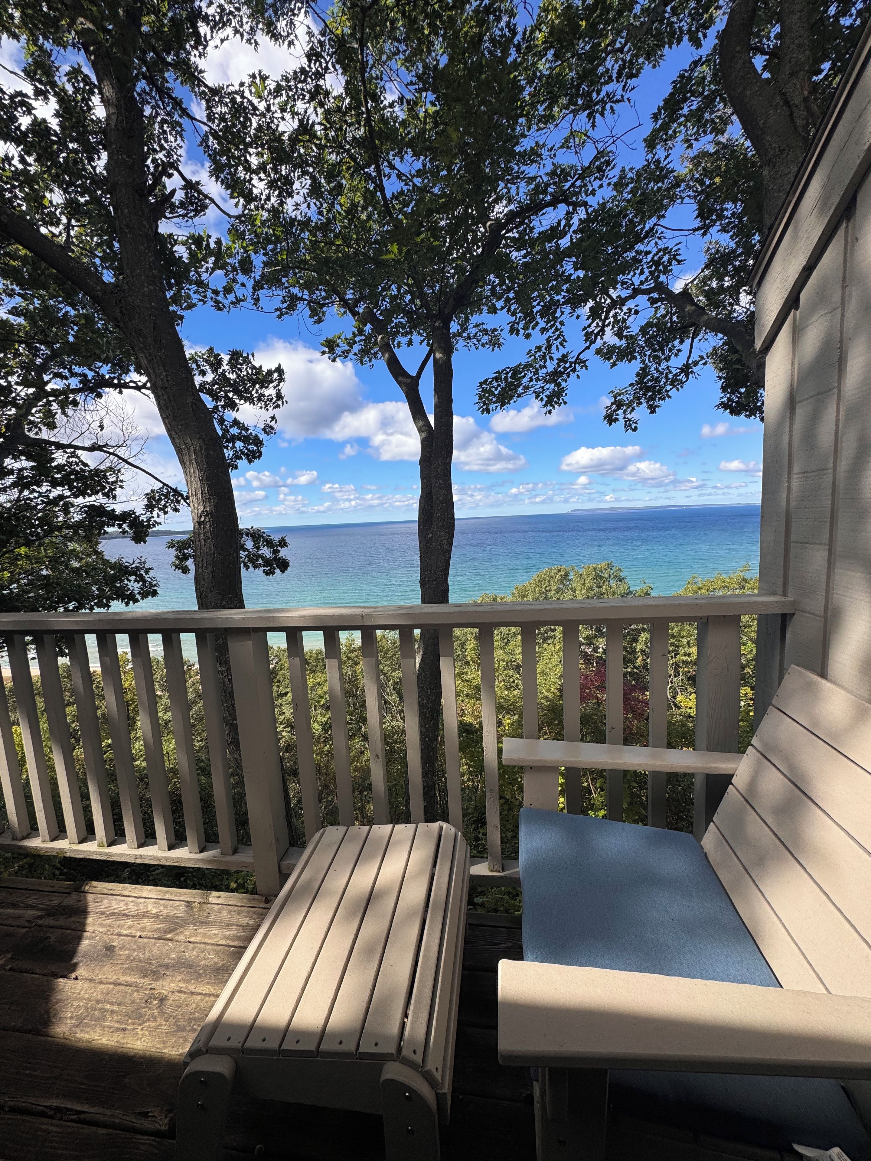Une terrasse en bois avec un banc et une table, donnant sur une étendue d’eau et des arbres.