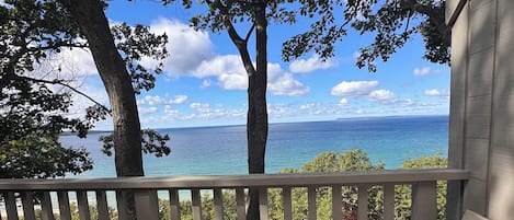 Eine Holzterrasse mit einer Bank und einem Tisch, mit Blick auf ein Gewässer und Bäume.