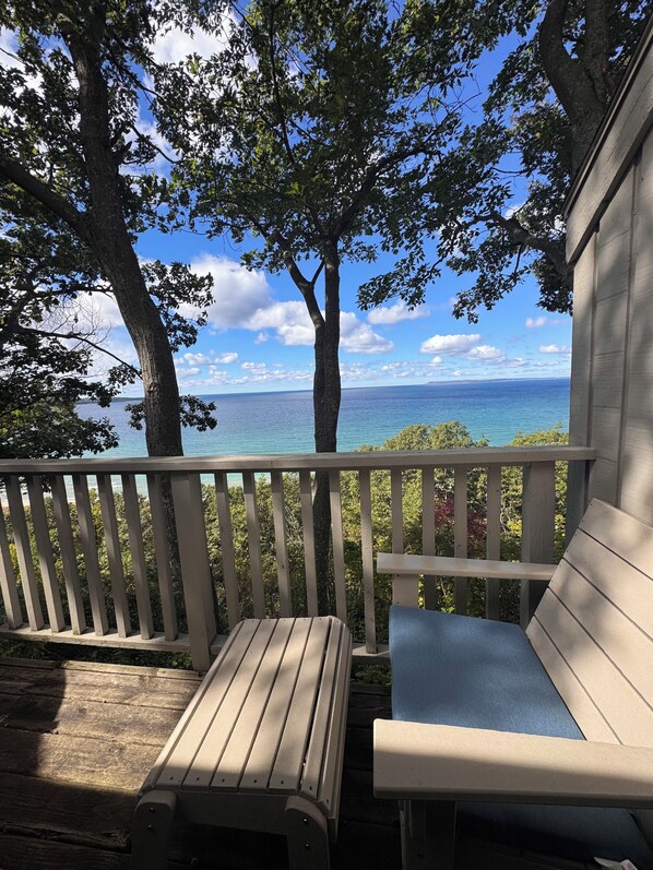 A wooden deck with a bench and a table, overlooking a body of water and trees.