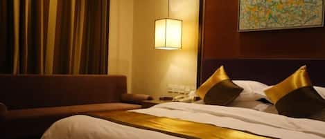 Una habitación de hotel con cama, sofá, lámpara y un cuadro en la pared.
