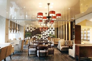 Un moderno vestíbulo de hotel con una imponente escalera, varias zonas de estar y un candelabro.