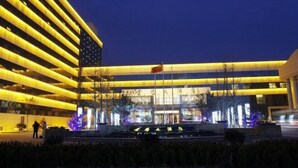 Ein modernes Hotel mit einer großen US-amerikanischen Flagge, einem gut beleuchteten Eingangsbereich und einer angelegten Grünfläche mit einem Brunnen.