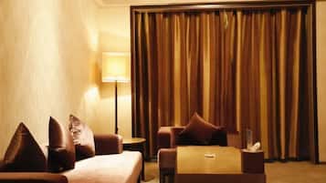 A hotel room with a bed, two sofas, a small table, a lamp, and a curtain.