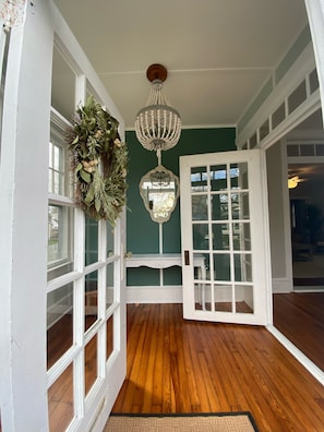 Una habitación con suelo de madera, ventanas de marco blanco, pared verde y una araña.