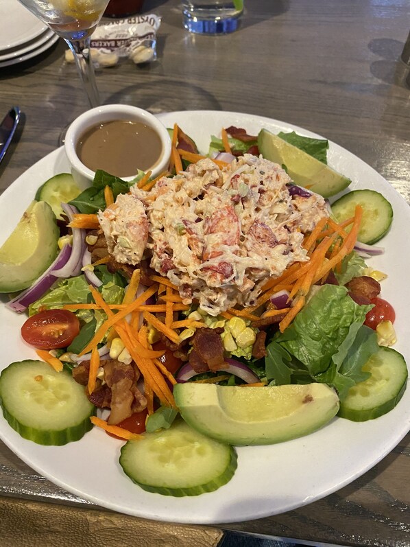 Ein Salat mit Avocado, Speck und Dressing auf einem weißen Teller.