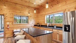 A wooden cabin kitchen with a central island, stainless steel appliances, and large windows. - Ridgeline Retreat w/ Heated Pool, Hot Tub + Views | Sleeps 12 (Sevierville)