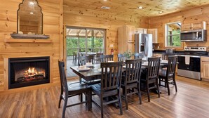A wooden cabin interior with a dining area, kitchen, and fireplace. - Ridgeline Retreat w/ Heated Pool, Hot Tub + Views | Sleeps 12 (Sevierville)