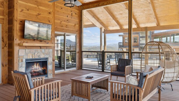 A wooden deck with a fireplace, seating area, and large windows offering mountain views. - Ridgeline Retreat w/ Heated Pool, Hot Tub + Views | Sleeps 12 (Sevierville)