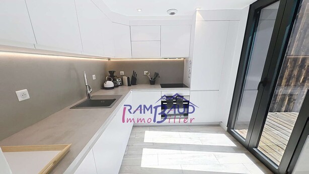 A modern kitchen with white cabinetry, a black countertop, and a built-in oven. There is a window providing natural light and a view of the outdoors.