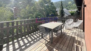 A wooden deck with a table and chairs, overlooking a mountainous landscape.
