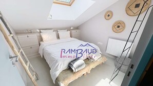 A bedroom with a bed, a skylight, a wooden ladder, and a wall-mounted shelf.