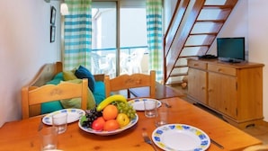 A dining area with a wooden table set for two, a fruit plate, and a television on a wooden cabinet. - Edificio Tamarius by Interhome (L'Estartit)