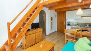 A compact living space with a wooden staircase, a kitchenette, a dining area, and a small seating area with a blue cushion. - Edificio Tamarius by Interhome (L'Estartit)