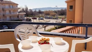 A balcony with a round table and chairs, a fruit bowl, and a view of a parking area and buildings. - Edificio Tamarius by Interhome (L'Estartit)