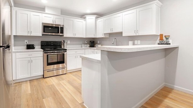 Een moderne keuken met witte kasten, roestvrijstalen apparatuur en een houten vloer.