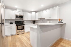 A modern kitchen with white cabinets, stainless steel appliances, and a wooden floor.