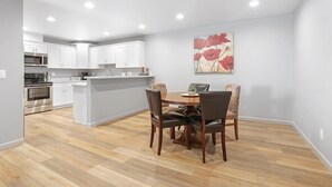 Een moderne keuken met witte kasten, een centraal eiland en een eethoek met tafel en stoelen.