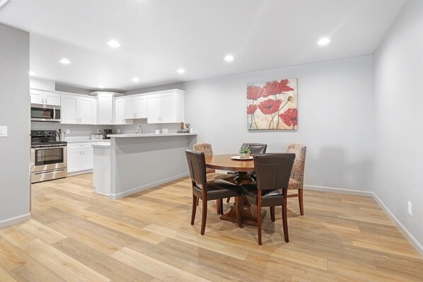 A modern kitchen with white cabinets, a central island, and a dining area with a table and chairs.