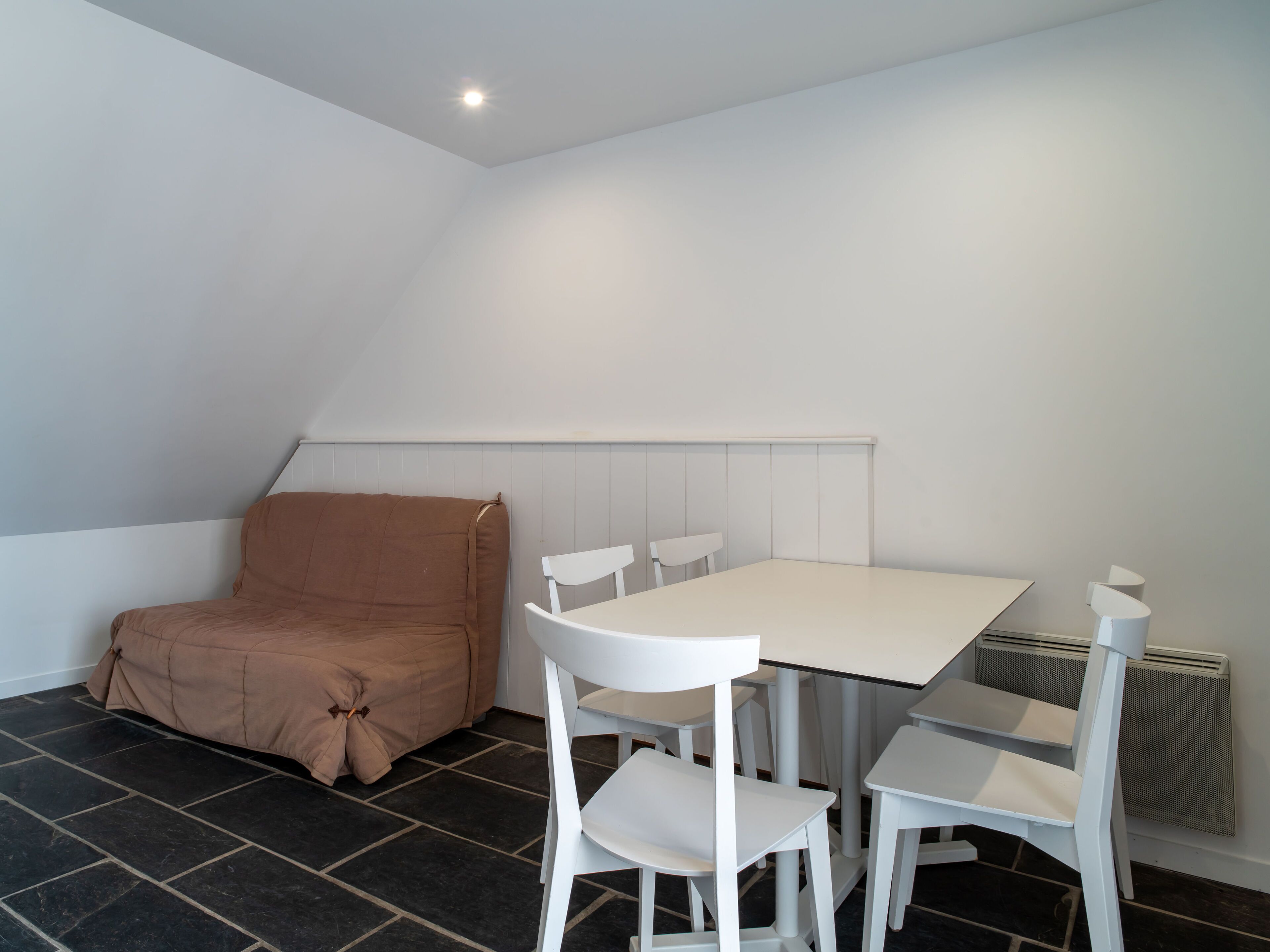 Una habitación pequeña y moderna con una mesa y sillas blancas, un sofá marrón y un radiador.