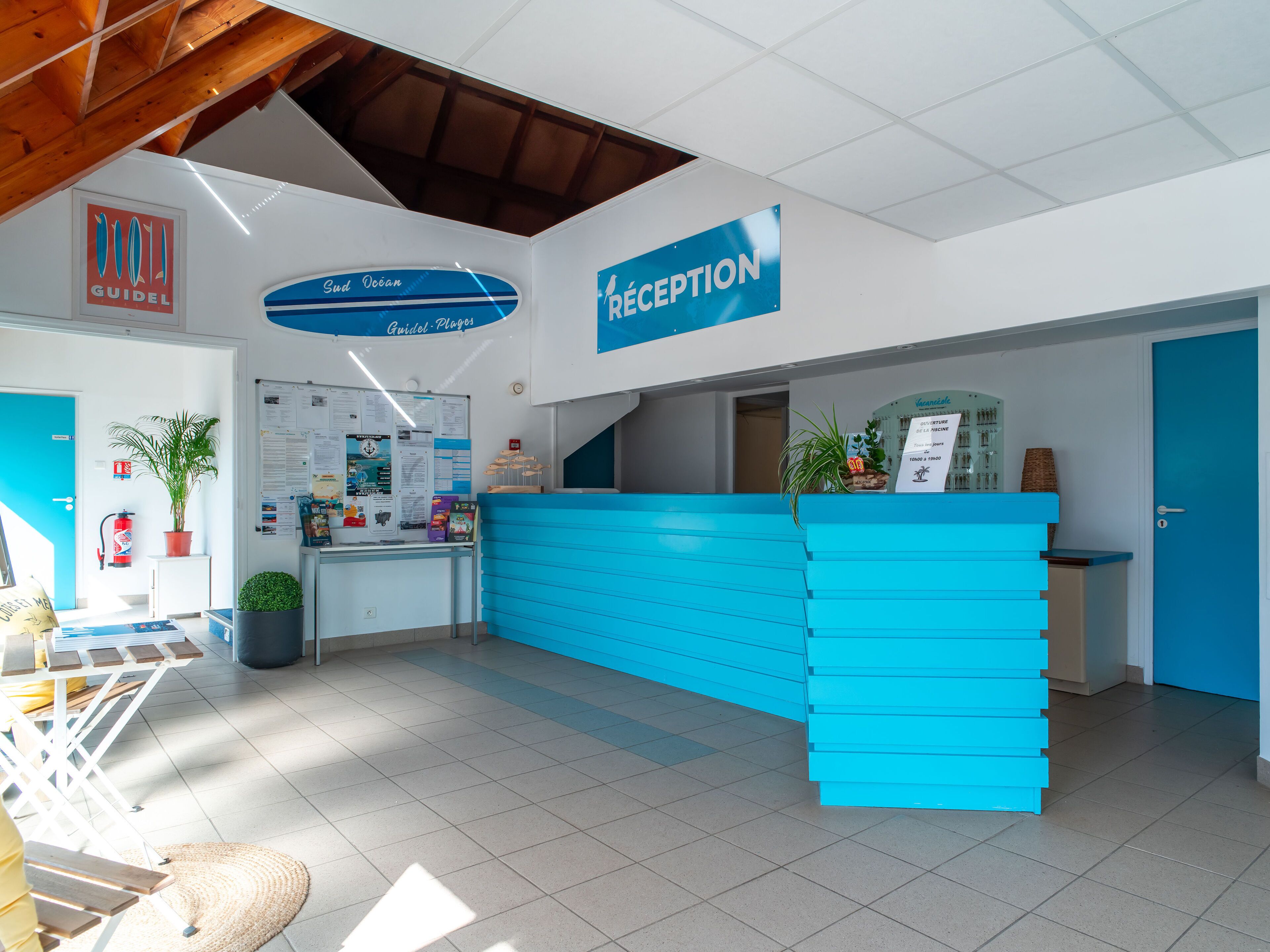 A reception area with a blue counter, a sign for 'Guidel Plages', and a reception sign.