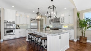 A spacious kitchen with white cabinetry, stainless steel appliances, a large island with bar stools, and pendant lighting. - Wine Country Retreat • Pool, Spa, Views (Temecula)
