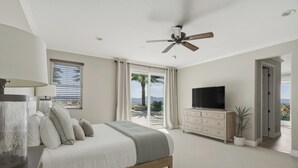A bedroom with a bed, a TV, a ceiling fan, a window with curtains, and a view of palm trees. - Wine Country Retreat • Pool, Spa, Views (Temecula)