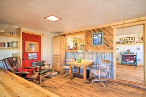 Una habitación acogedora con suelo de madera, una puerta roja y un comedor con mesa y sillas.